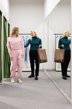 Mother helping daughter choosing clothes in fitting room in store