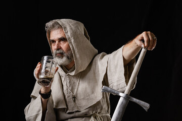 An excited warrior monk holds a sword in one hand and a glass of dark ale in the other.