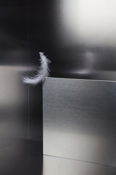 White feather on corner of silver sheet avoiding falling in balance