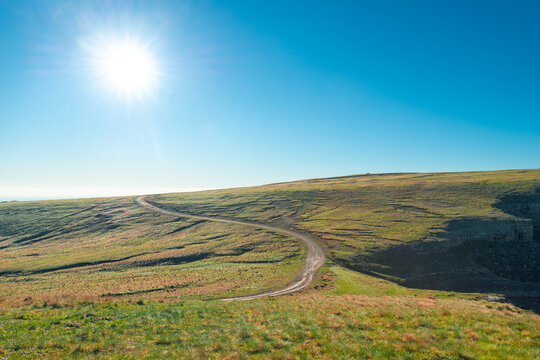 A beautiful landscape with a dirt road leading to a low hill with scant alpine vegetation in sunny weather