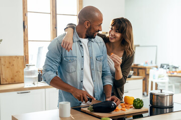 Beautiful and romantic couple hugging while cutting vegetables in the kitchen at home