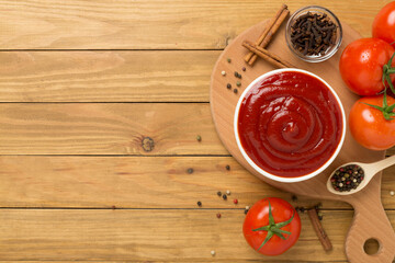 Delicious ketchup with spices and tomatoes on wooden background, top view