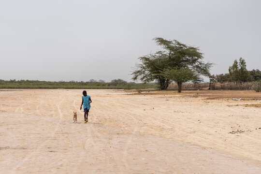Young african child running with dog in arid landscape of senegal