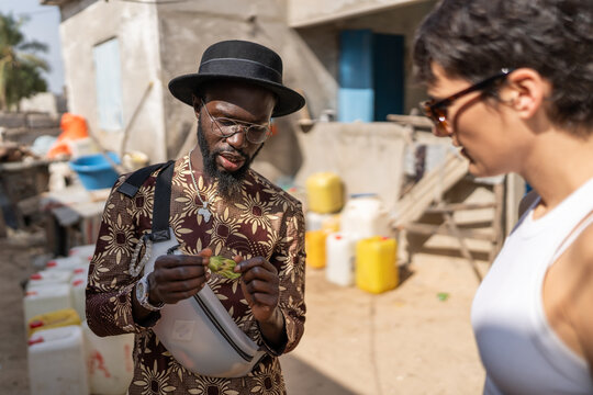 Local senegalese man wearing a hat and showing a plant to a tourist