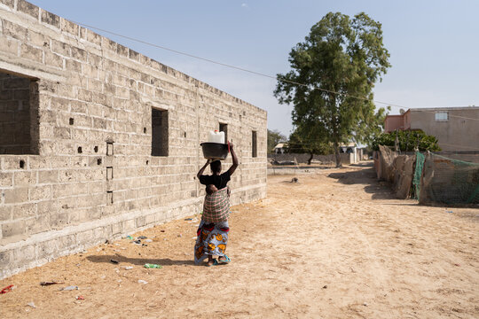 African woman is walking in a rural village carrying water and a baby