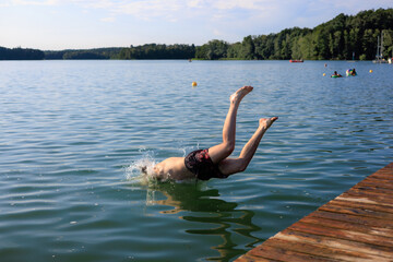 A guy clumsily dives into a lake from a pier. Legs spread.