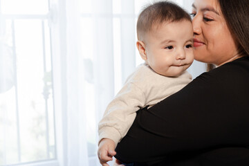 Detail of 6 months old baby in his mother's arms - hispanic mother kissing her baby while spending mother and son time - single mother with her baby at home
