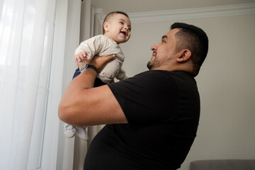 Father with his son smiling at home - young man enjoying his fatherhood with his 6 month old baby -...