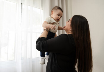 Happy hispanic mom lifting her adorable baby up in the air