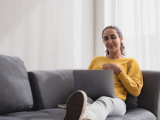 Fototapeta premium Portrait latin american business woman one person smile happy sitting sofa and looking laptop plan online job work newproject along with looking success future in living room office