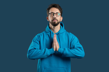 A young man with glasses is engaged in mindfulness meditation, wearing a blue hoodie. His hands are...