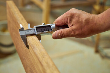 a man in a home carpentry workshop measures boards with a caliper close-up of hands