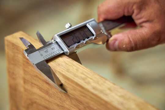 a man in a home carpentry workshop measures boards with a caliper close-up of hands