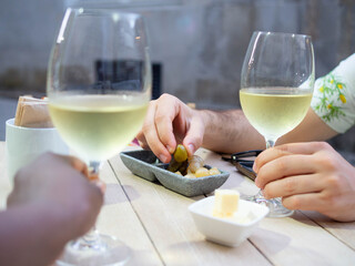 Two hands taking their glasses of white wine and eating olives on the terrace of a bar