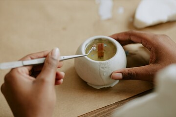 Hands skillfully crafting handmade candle. Person holding a tool, working on intricate details with...