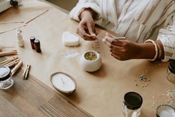Focused image of hands engaged in meticulous candle-making process, using natural wax and essential...
