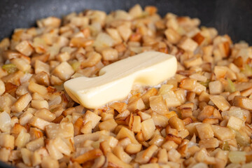 Frying pan full of chopped, fresh bay boletes and boletus or king oyster mushrooms or eryngii (Pleurotus eryngii) during the process of frying with piece of butter. Gas stove in the background.