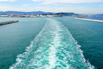 Wide turbulent white foam water trail behind a large cruise ship leaving the port of Barcelona