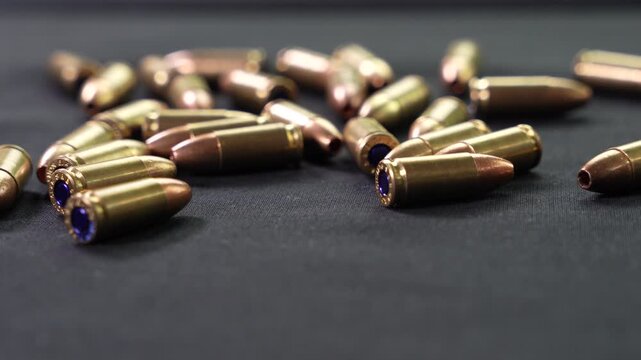 A hand picks up a 9mm cartridge amidst a handful of ammunition scattered on a black surface
