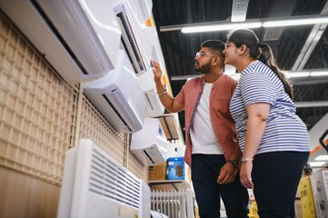 Young indian couple, satisfied customers choosing air conditioner in appliances store