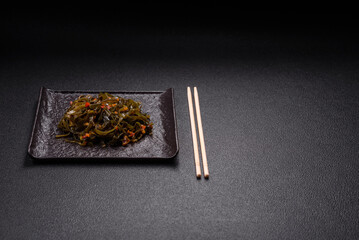 Delicious marinated seaweed with paprika, spices and salt on a dark concrete background