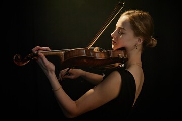 Side view medium shot of graceful female musician sensually playing violin under projector contrast...