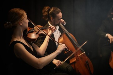 Side view of chamber female and male musicians playing violin and cello with passion during...