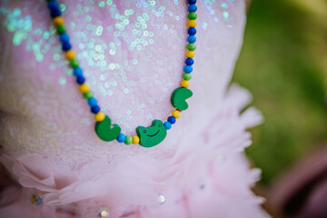 Valmiera, Latvia - July 15, 2024 - Close-up of a colorful beaded necklace with green frog and lily pad charms on a pink sequined dress, highlighting the playful design.