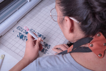 Young woman removes excess material with weeding tool, cutting plotter workplace.