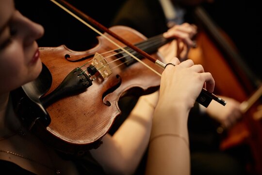 Close up on hand of unrecognizable female orchestra musician playing violin with bow during concert on stage, focus on hand and tailpiece