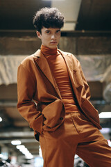 Stylish young man in brown outfit posing confidently in an industrial setting