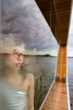 A girl looking out from behind the glass of a sauna