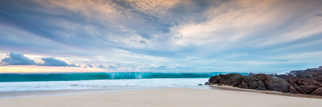 Dramatic skies and large wave curl on sandy beach