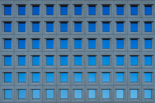 Concrete building facade with blue sky reflected through its windows 