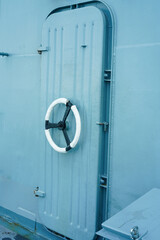 The rotating hold on iron door in old military war submarine warship ship, blue background with copy space.Vertical. © surasak