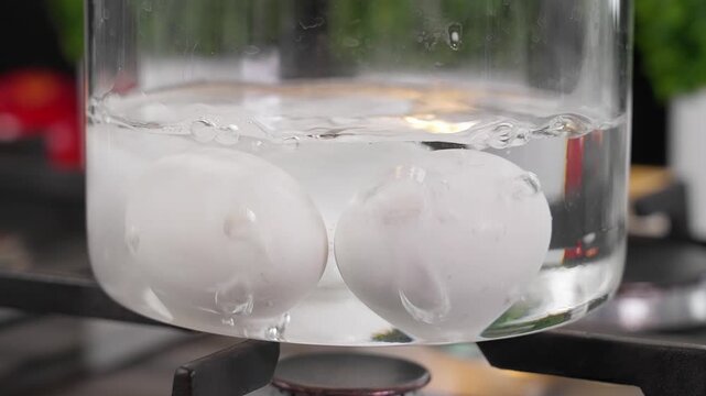 Chicken eggs are boiled on the fire in a glass saucepan. Boiling white chicken eggs in a glass container. Dietary product, healthy food, healthy. Close-up, front view