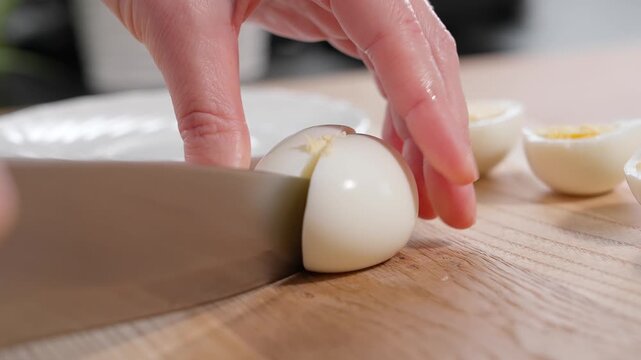 Chef cuts chicken egg in half with sharp knife, wooden board. Protein food, protein, dietary product, pie filling. Close-up, macro, side view