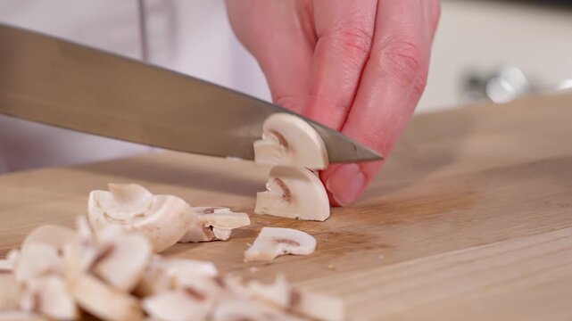 Close-up chef using a sharp knife slices champignon mushrooms, wooden board Preparation for salads, mini pizza with mushrooms, pie, appetizer, side view, macro