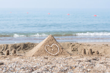 Sand pyramid with shells in a heart shape on its side built on the beach, sea in the background...