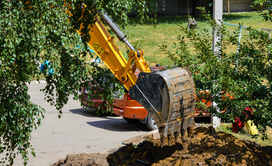 excavator bucket digs a hole in the yard in the city on the street
