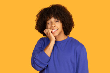 A young man with curly hair is nervously biting his nails while wearing a blue shirt. The bright...