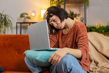 Angry woman using laptop typing browsing working, loses becoming surprised sudden lottery results bad news fortune loss fail computer virus. Upset Caucasian girl on couch in living room at home.