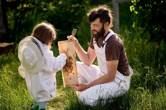 A young dad beekeeper teaching his little daughter on the apiary