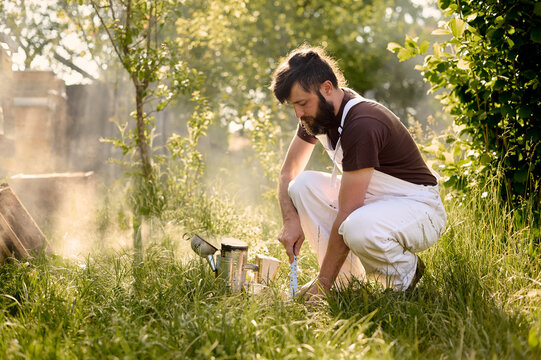 A male beekeeper in protective uniform with smoker in apiary