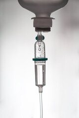  detailed image of an intravenous (IV) drip with clear liquid and air bubbles in a medical environment.