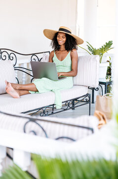 Woman in sun hat works on laptop on outdoor couch