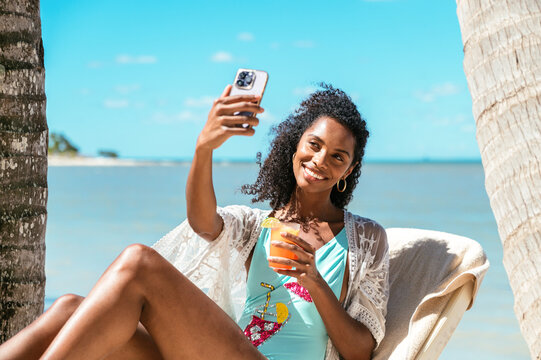 Happy woman takes a selfie at tropical beach with cocktail