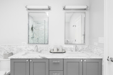 A bathroom detail with a grey cabinet, white marble countertop, and lights mounted above the...