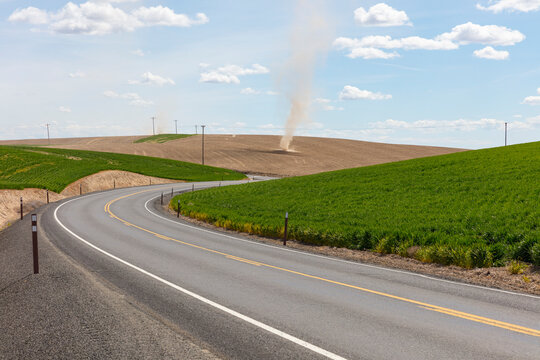 Small twisters forming over farmland, road in foreground