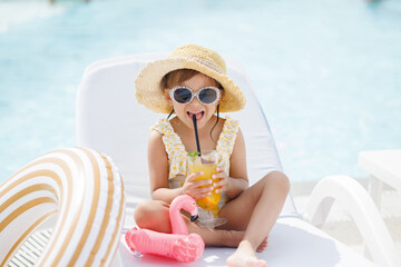 Funny cute girl drinks a cocktail on summer vacation. The child has fun on the beach. Cute baby in...
